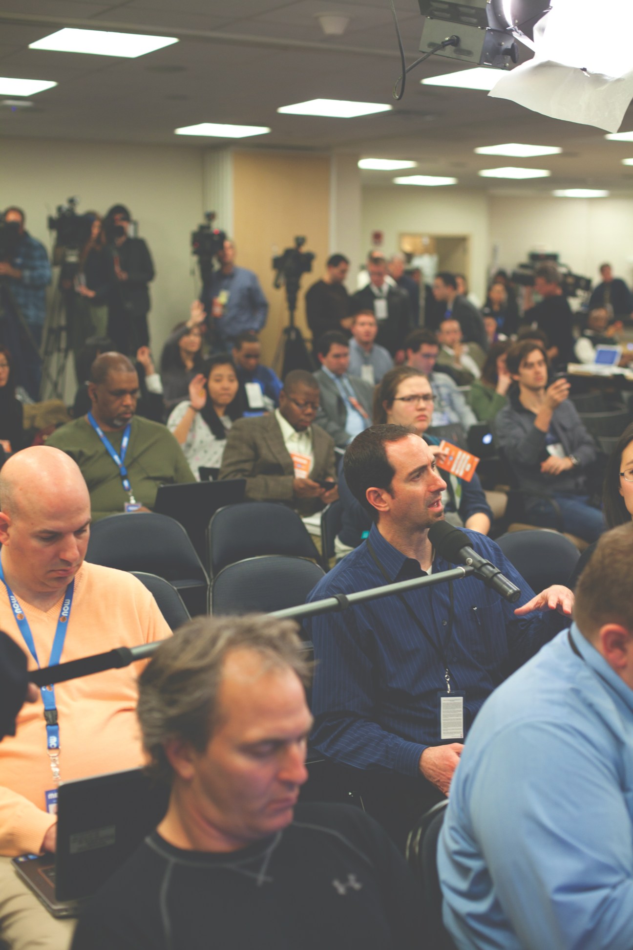 Sports journalists and media personnel seated at a post-match press conference with microphones and cameras.