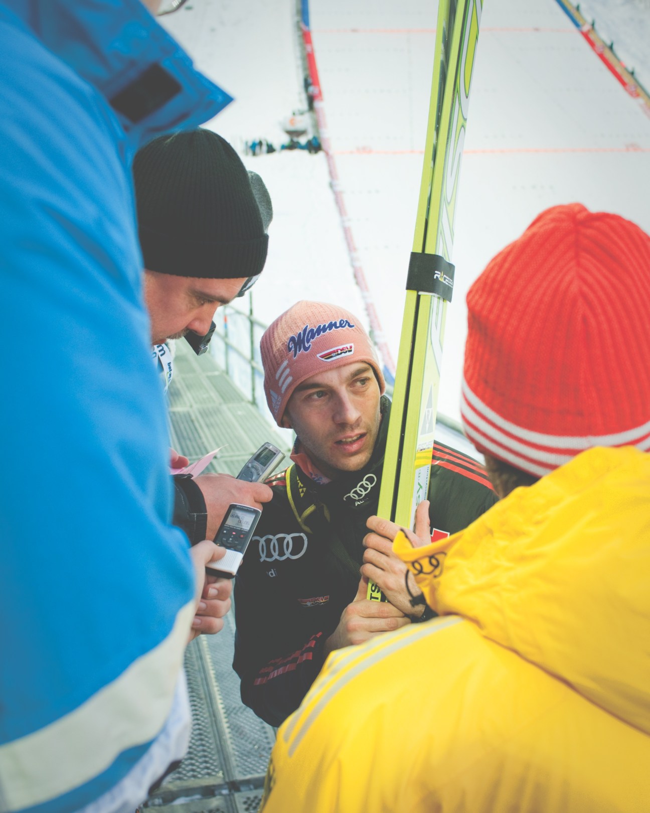 German ski jumper Michael Neumayer is interviewed by journalists holding microphones at a ski jumping competition.