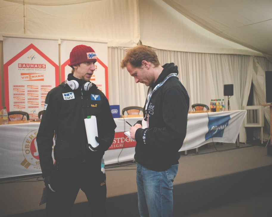 Thomas Hahn interviews Austrian ski jumper Martin Koch at a ski-jumping competition press area.