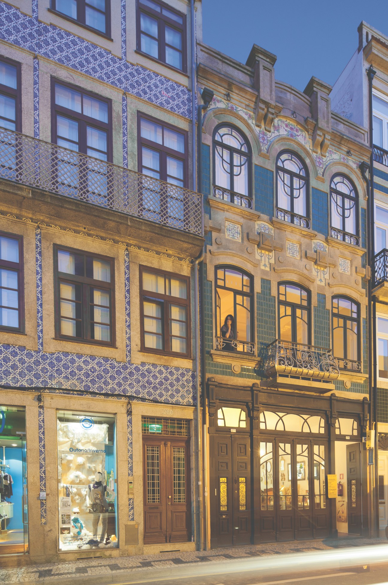 Historic Portuguese building facade with blue and white azulejo tiles, arched windows, and ground-floor storefronts in Porto.