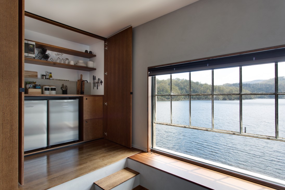 Modern hotel room with wooden cabinetry and floor-to-ceiling windows overlooking Lake St Clair in Tasmania.