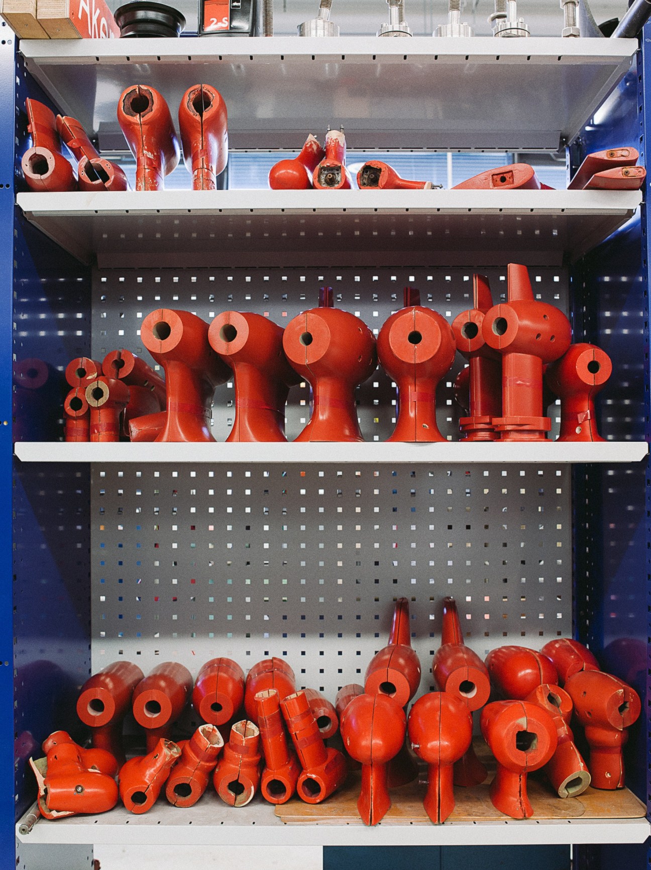 Red scale model ship propellers and components organized on blue shelving with pegboard backing.