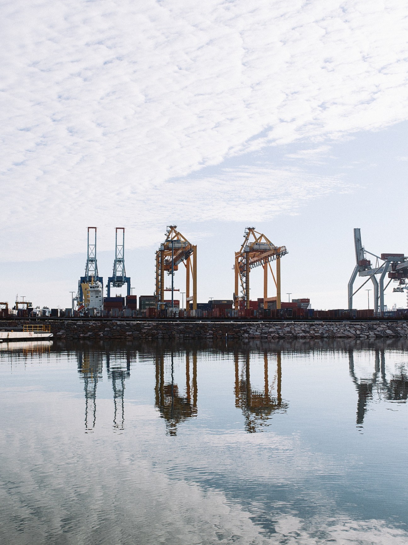 Industrial port cranes and container handling equipment reflected in calm water at Vuosaari container port, Helsinki.