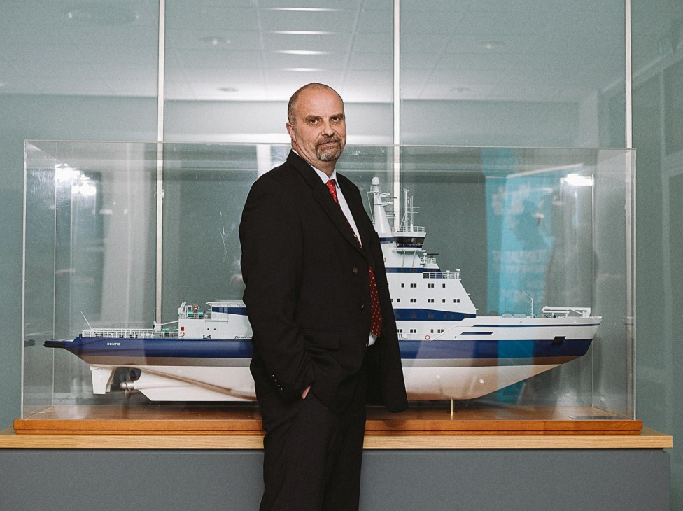 Jarkko Toivola, head of the Winter Navigation Unit at the Finnish Transport Agency, stands beside a scale model of an icebreaker ship in an office.