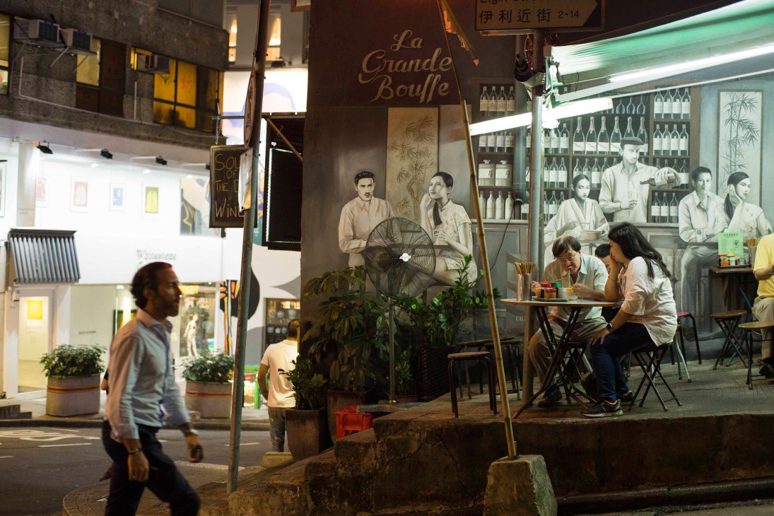 Street-food stall outside La Grande Bouffe restaurant on Hollywood Road at night with diners seated nearby.