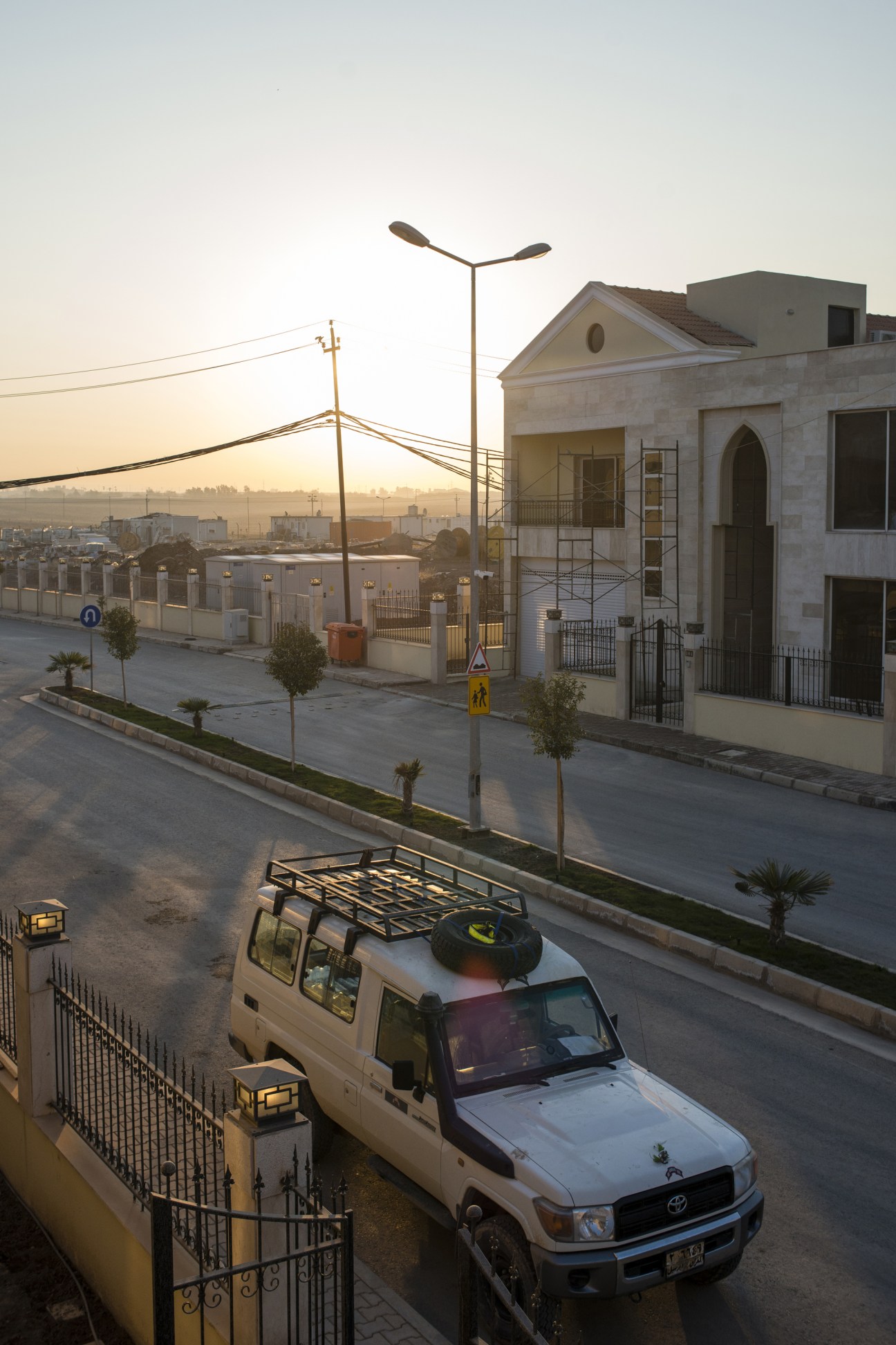 A white pickup truck parked on a newly constructed street in Erbil at dusk with modern buildings and city skyline in background.