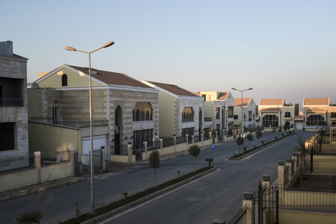 Empty new housing complex with uniform cream and stone buildings with orange-tiled roofs lining a quiet street in Erbil.