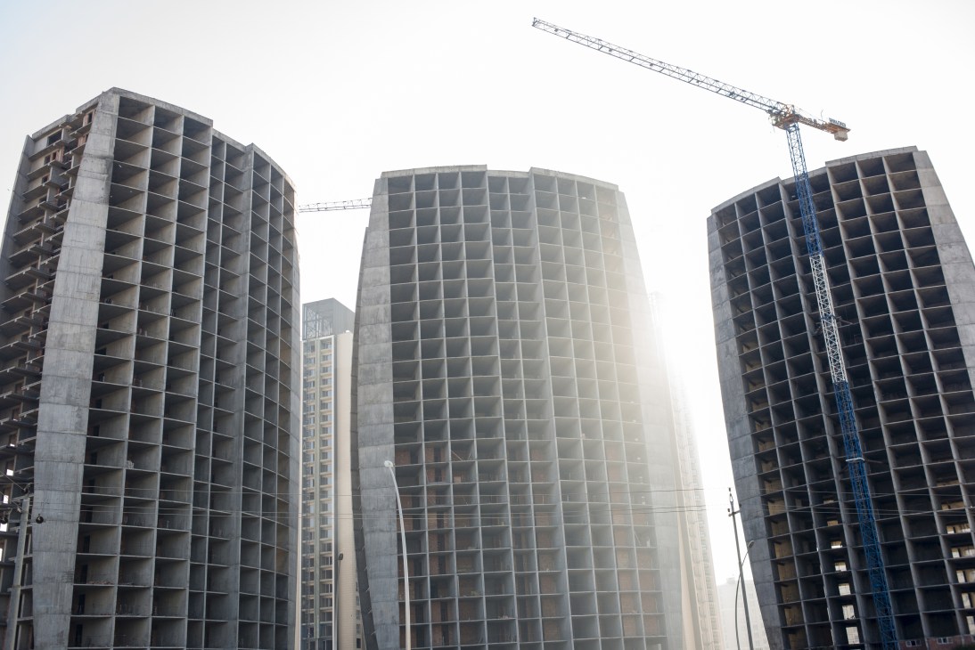 Half-finished luxury apartment and office buildings under construction in Erbil with a blue crane visible against the sky.