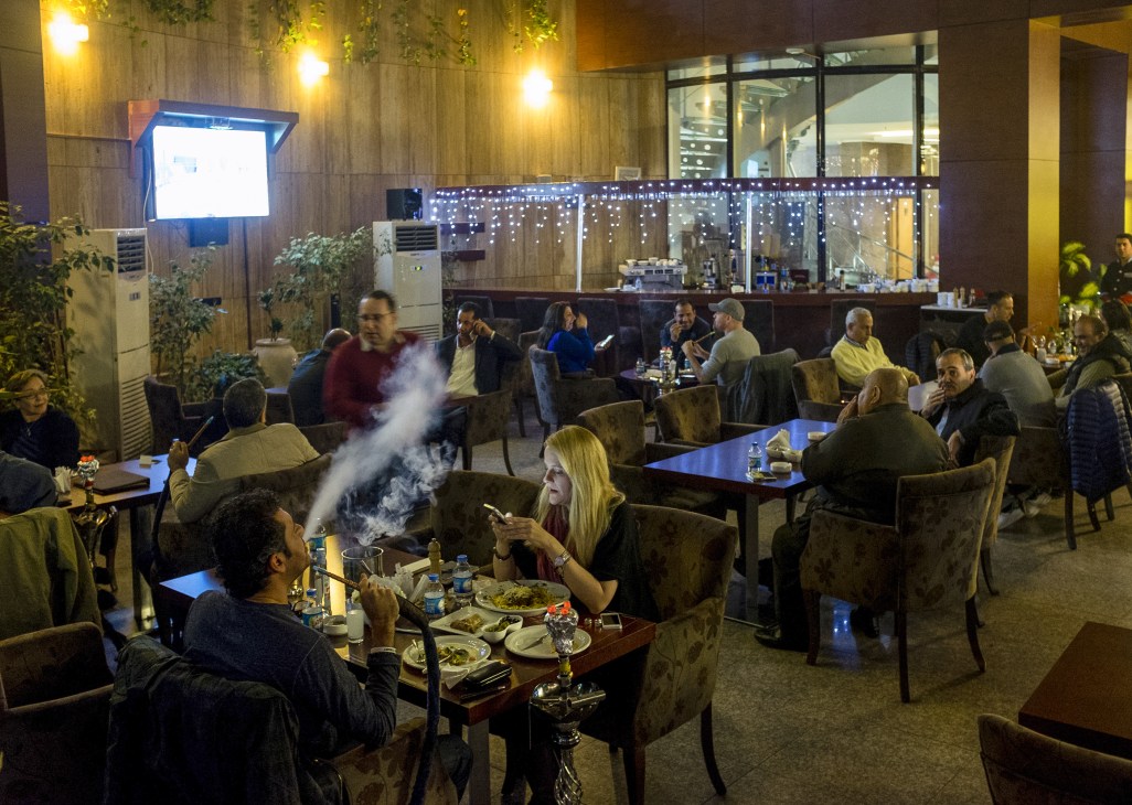 Journalists and locals dining and socializing in an indoor restaurant lounge during evening.