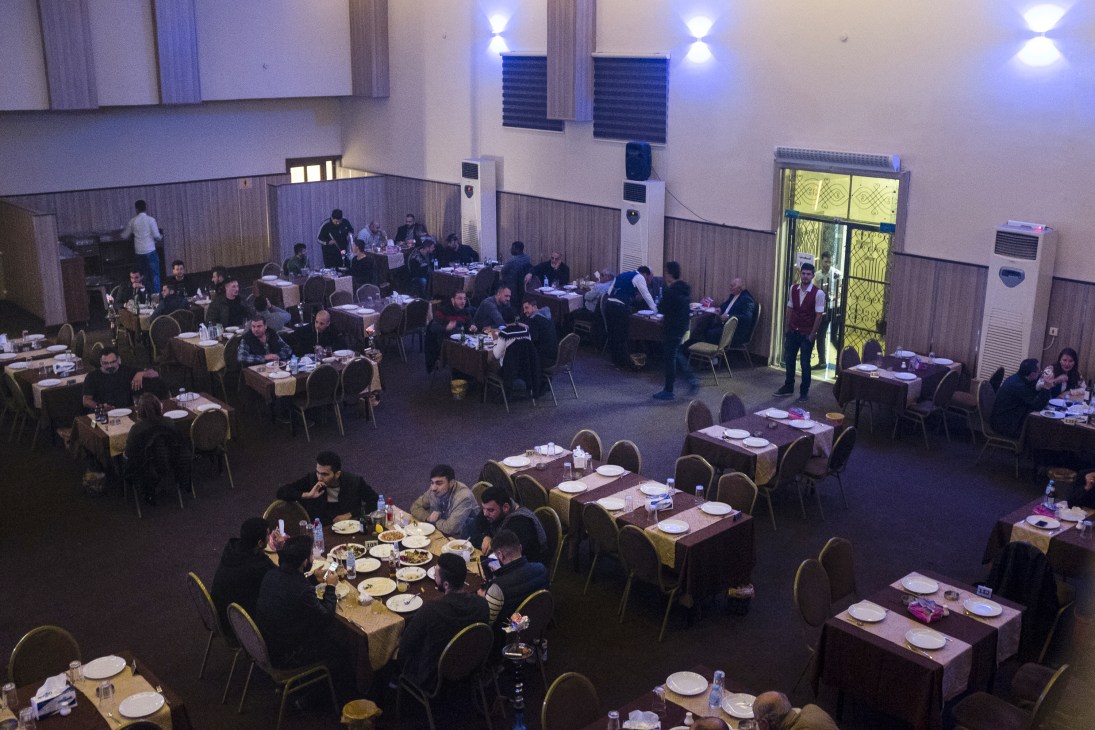 Interior of Teachers' Club restaurant in Erbil with journalists dining at tables during evening gathering.