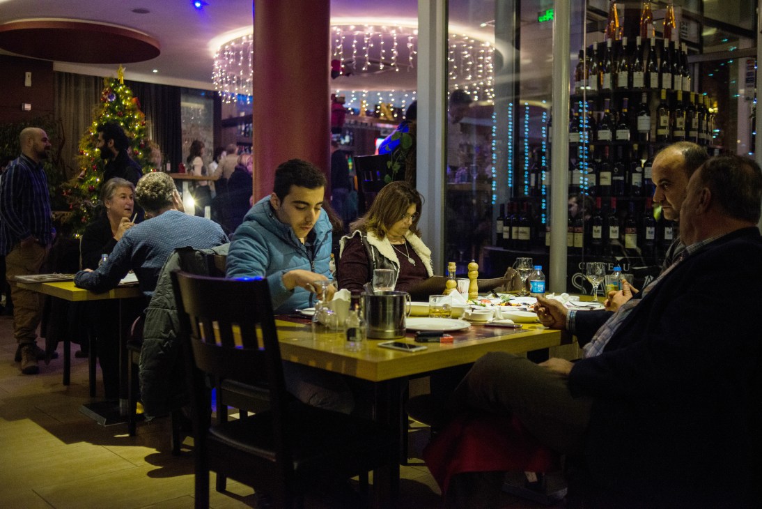 People dining and socializing in a modern restaurant with wine bottles displayed on illuminated shelves.