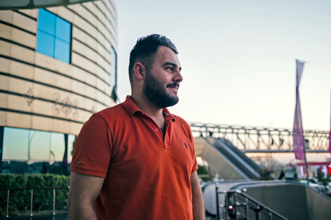 Fixer Ehsan Mamakani stands in profile wearing a red polo shirt outside a modern building in Erbil.