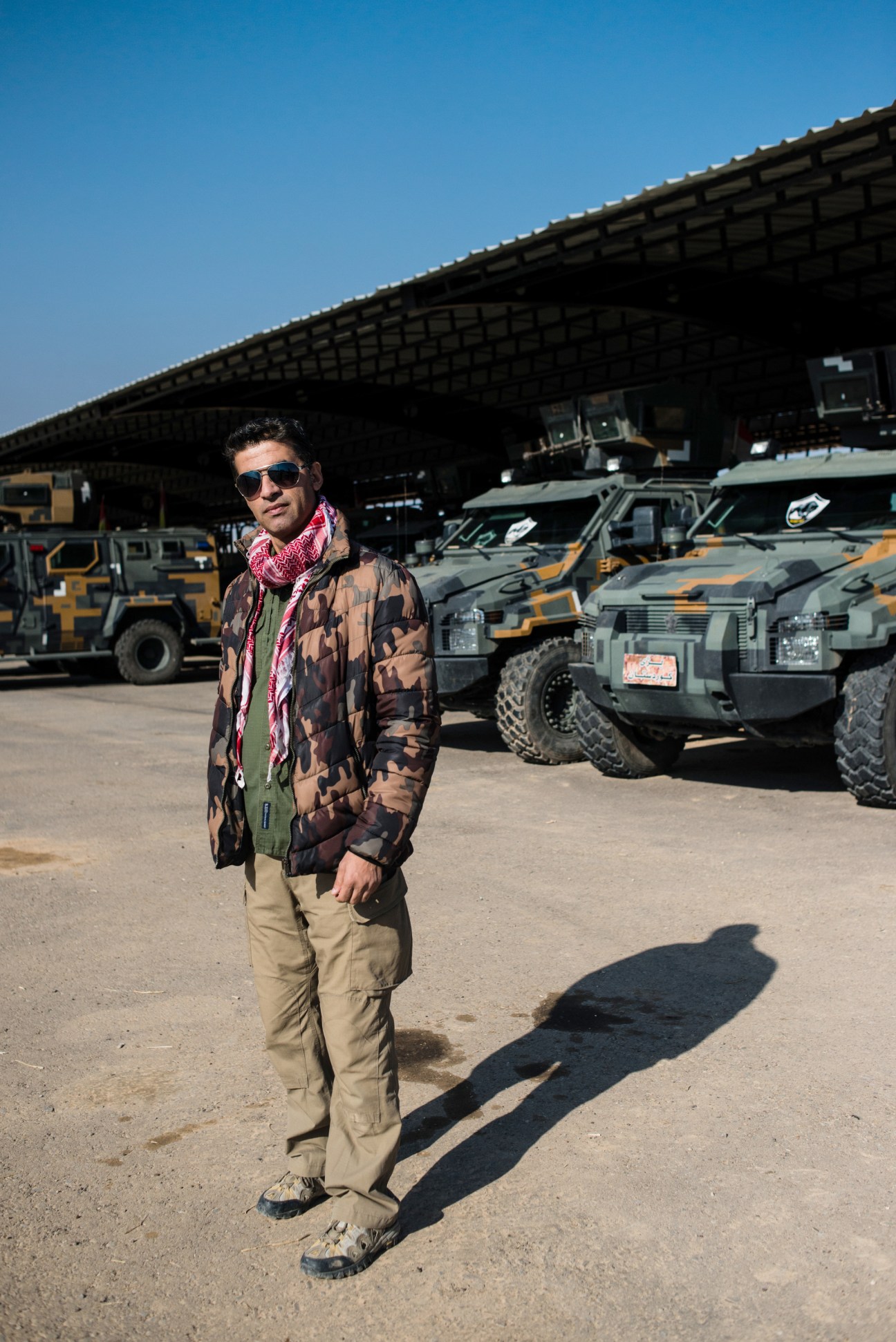 Kurdish fixer Hogar stands in front of military vehicles at a Peshmerga base.