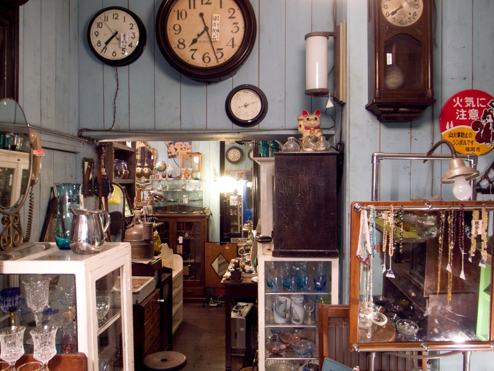 Interior of Akutokuya second-hand furniture shop displaying vintage clocks, glassware, wooden furniture and decorative items.