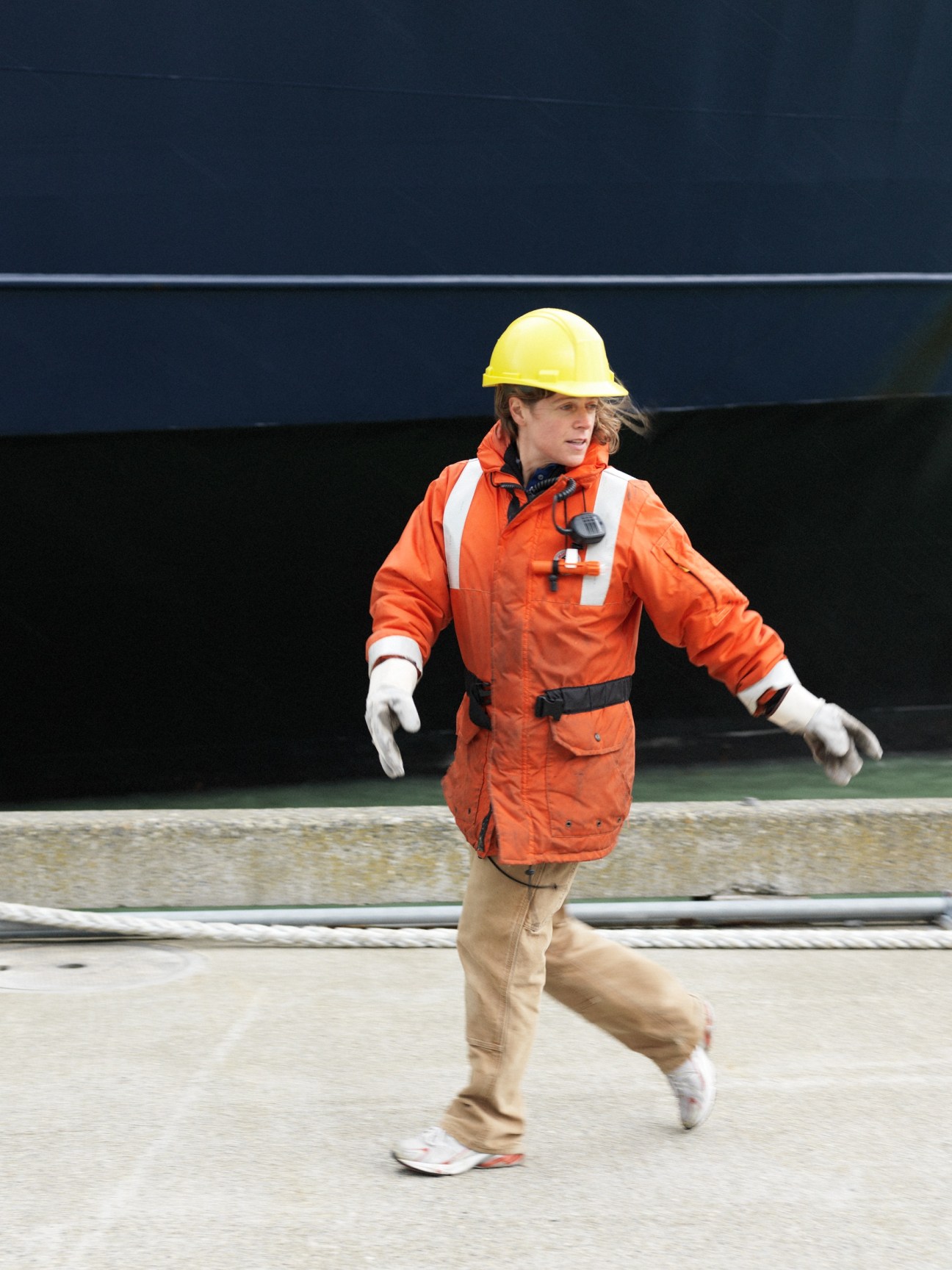 Ferry crew member in safety gear running on dock to catch mooring lines.