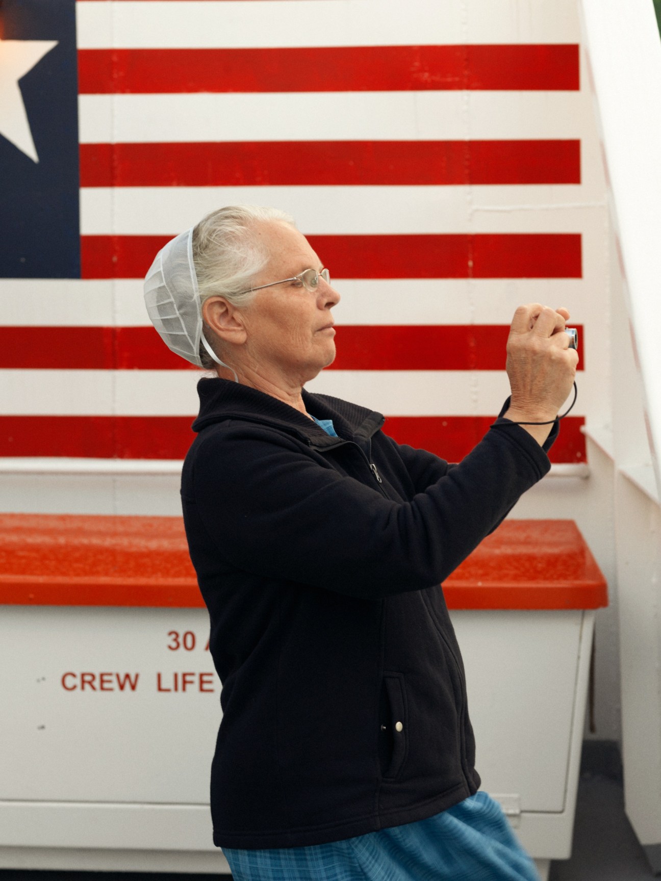 Passenger photographing Alaska scenery aboard the M/V Columbia ferry with American flag visible.