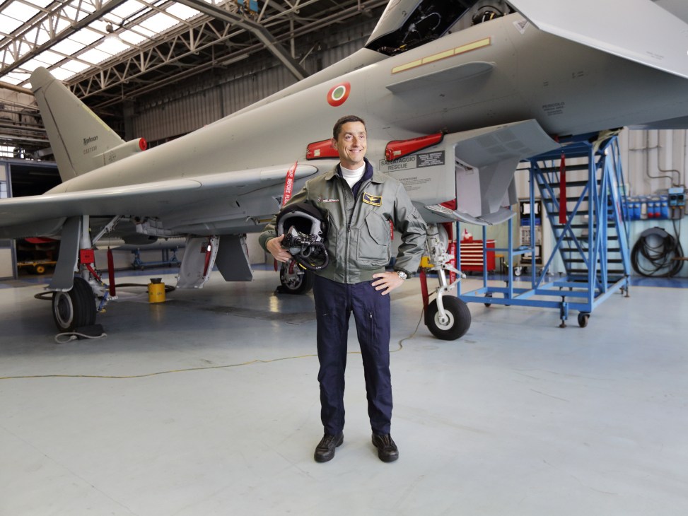 Marco Venanzetti, head of flight operations, stands in front of a Eurofighter Typhoon jet in a hangar holding a pilot's helmet.