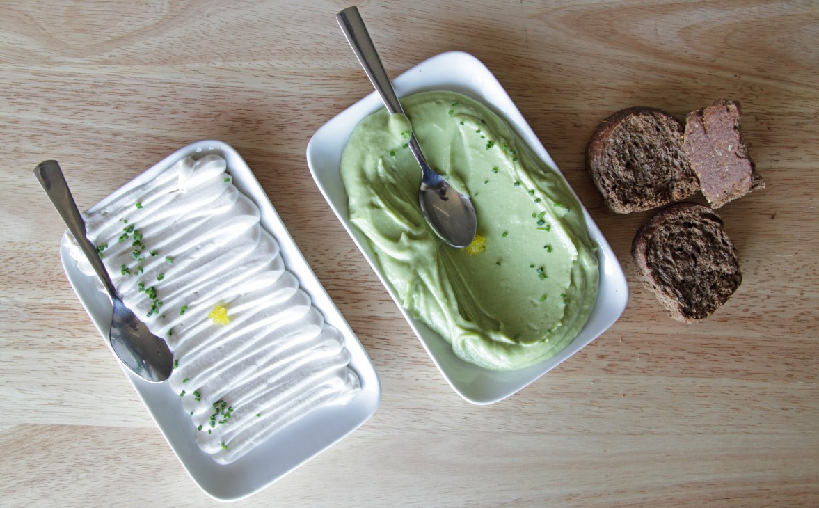Traditional Greek dishes including white cheese, green herb spread and dark bread on a wooden surface.
