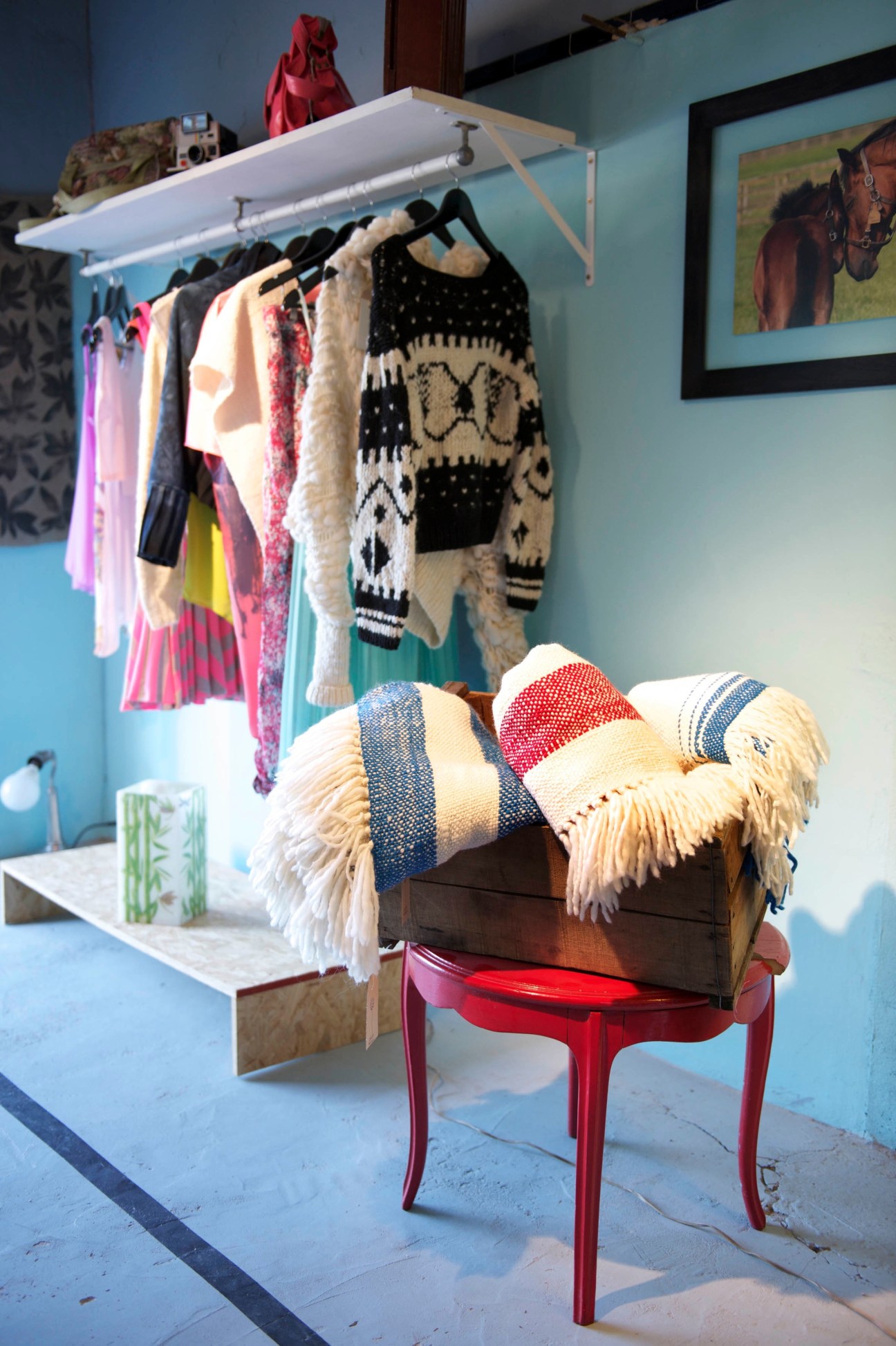 Interior of Alium design store displaying colorful clothing on wall rack and woven textiles on red chair.