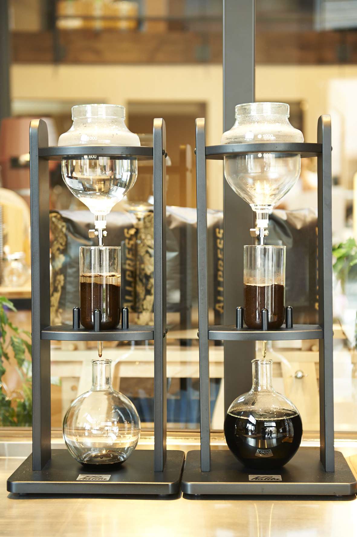Two black metal pour-over coffee brewing devices with glass vessels containing brewed coffee.