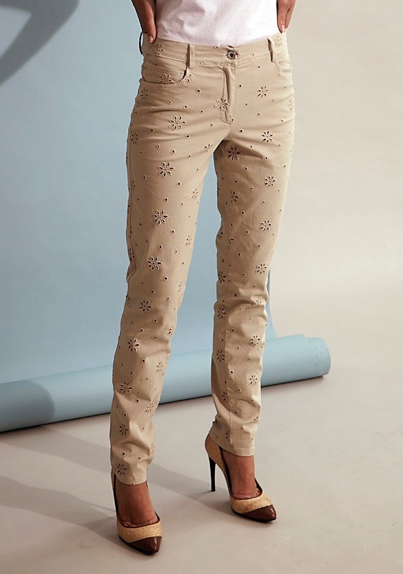 Beige trousers with embroidered floral print worn with brown heeled shoes.