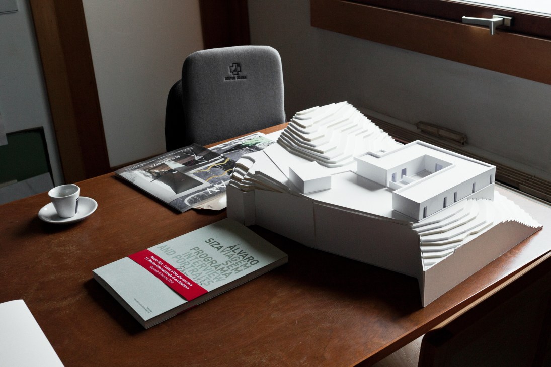 Architectural models and design materials displayed on a wooden desk in a meeting room.
