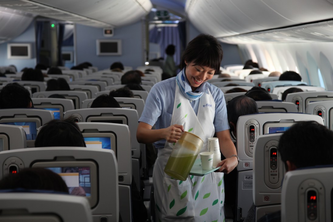 ANA flight attendant serving beverages inside the Boeing 787 cabin with rows of seats visible.