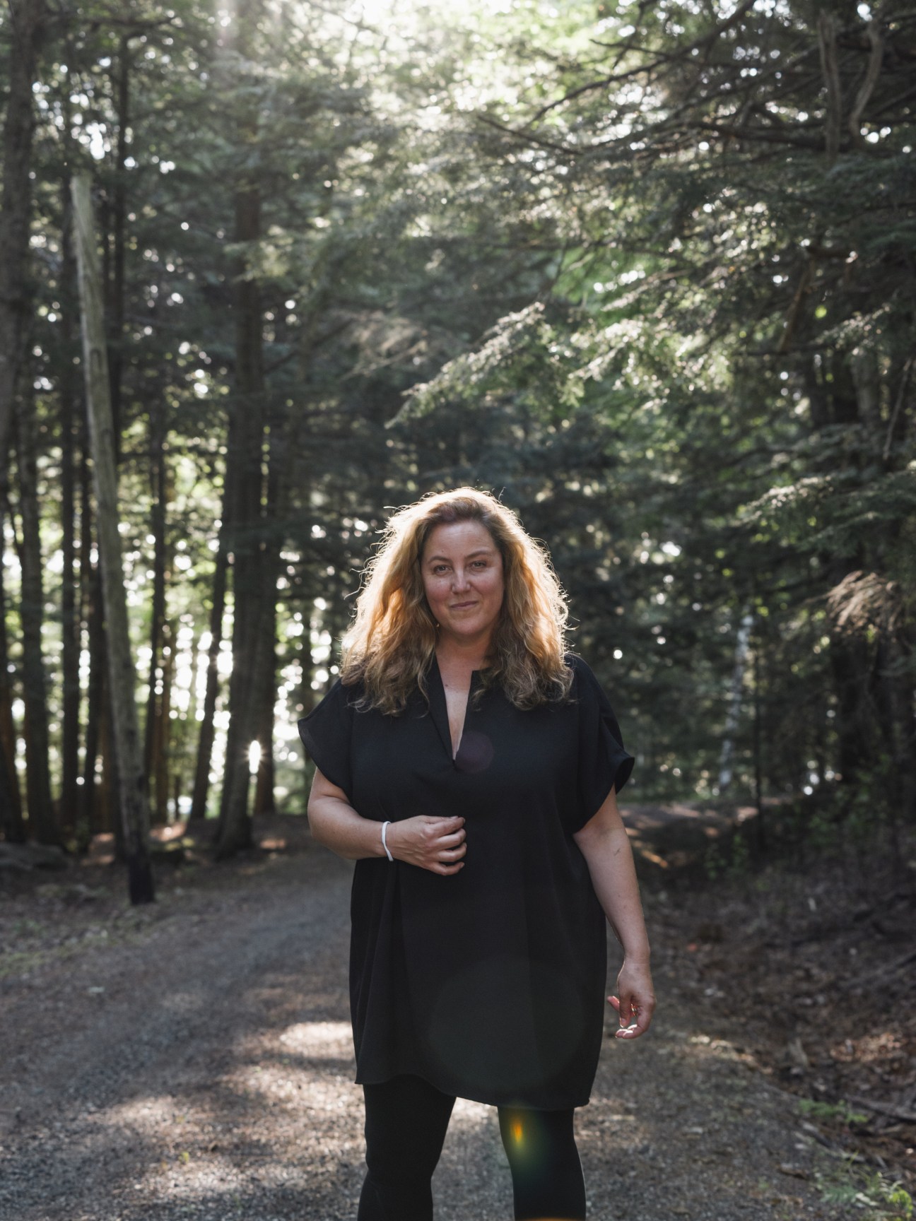 Anna Winger, creator of Deutschland 83, stands on a forest path wearing a black dress.
