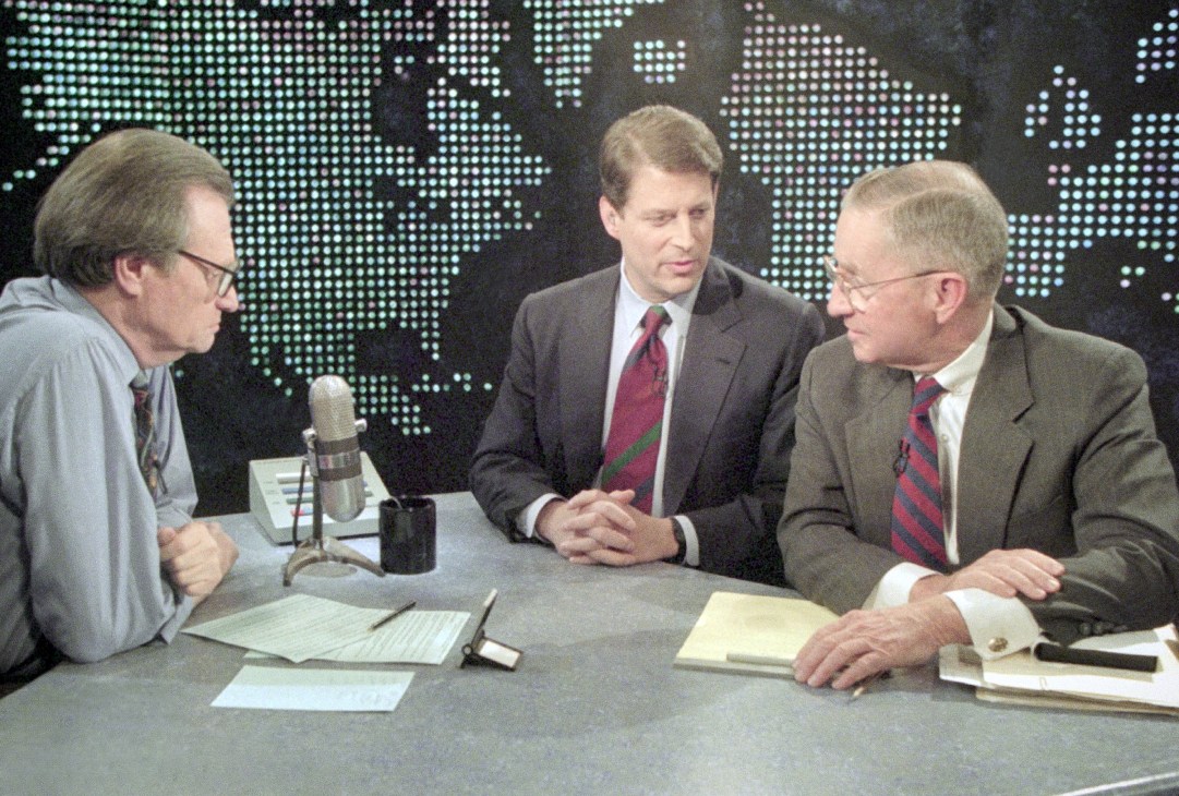 Three men in business attire at a TV studio desk with a world map backdrop during CNN's Larry King Live.