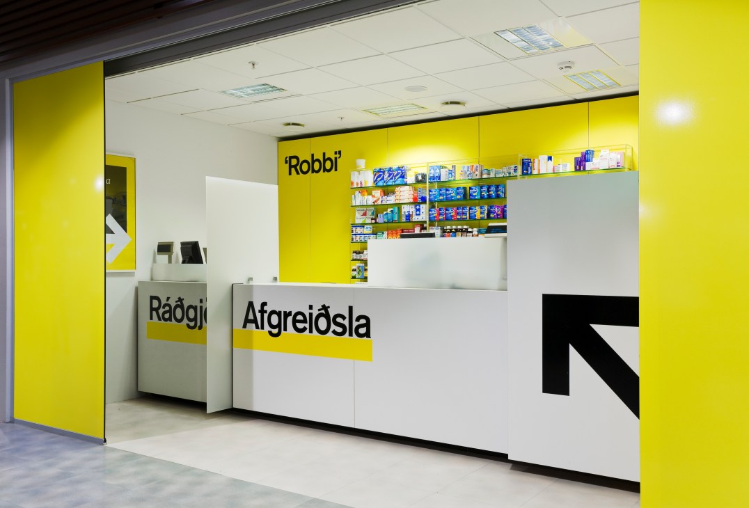 Bright yellow and white pharmacy interior with 'Afreiðsla' signage and product shelving.