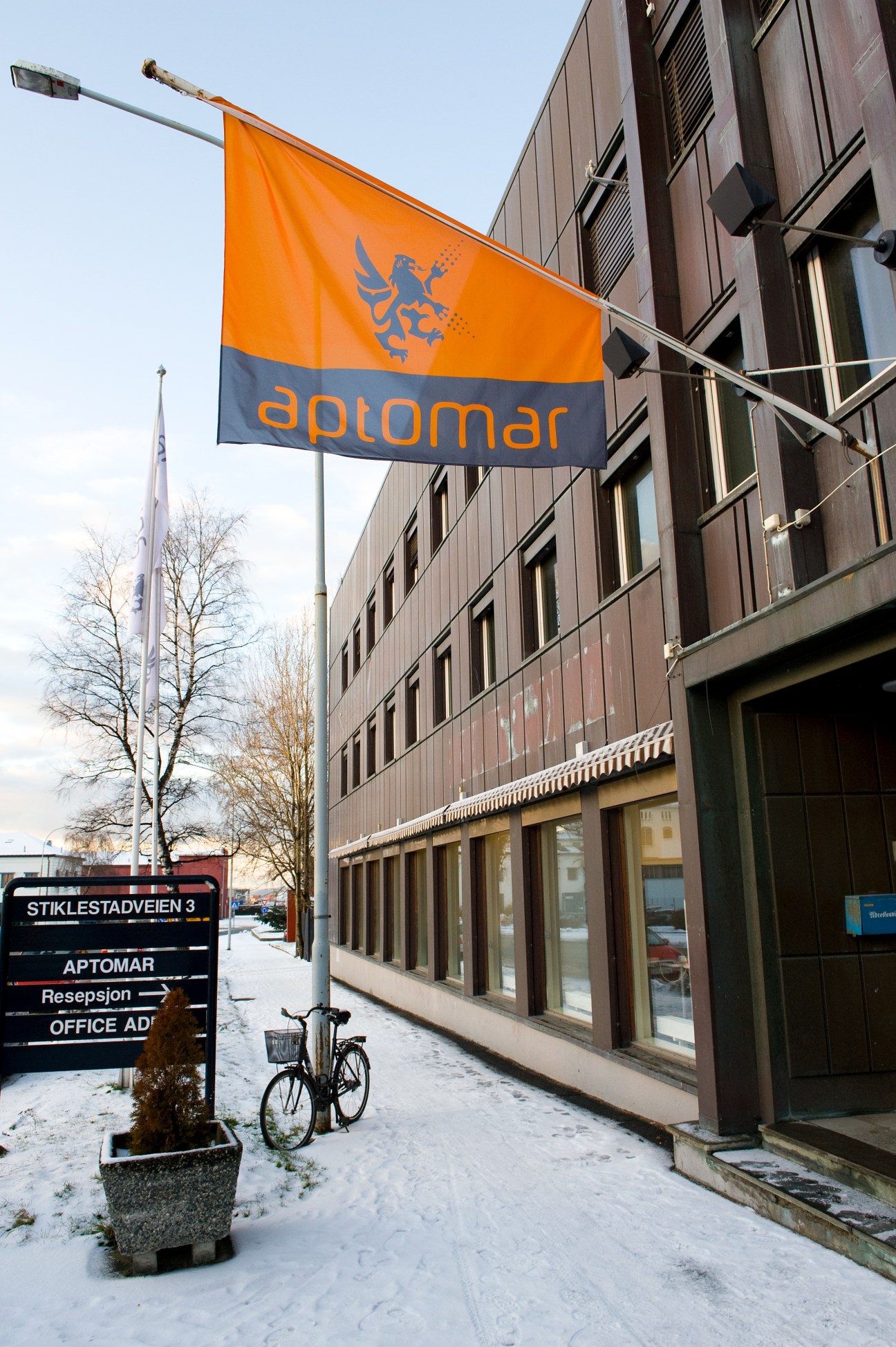 Aptomar's orange and navy flag with lion logo hanging outside their Trondheim office building.