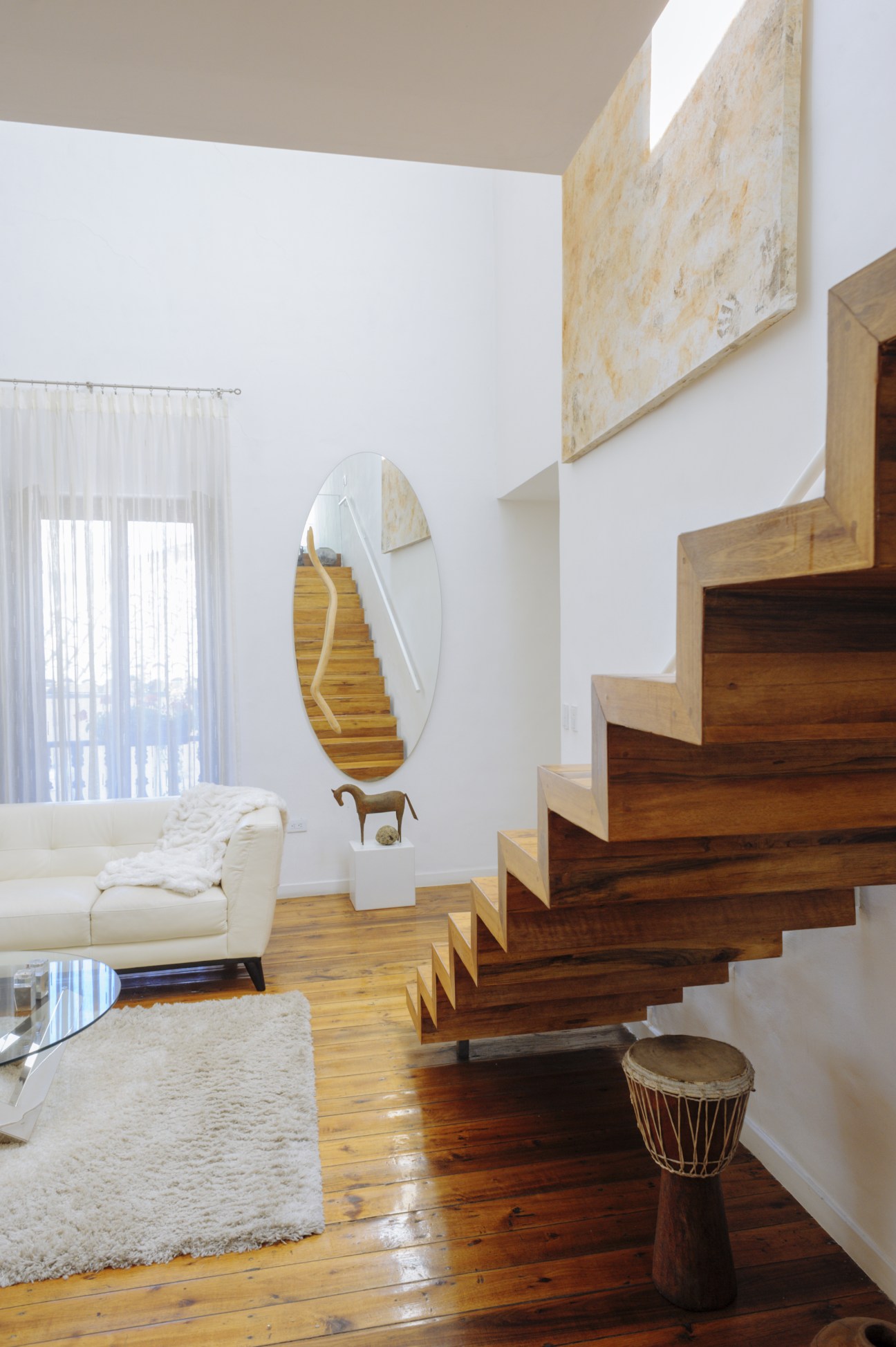 Modern interior with wooden staircase, white walls, cream sofa and oval mirror in a Cuenca home.