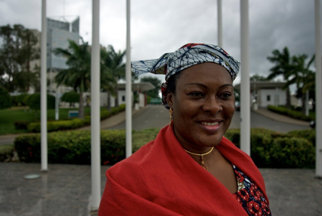 Ramatu Aliyu, an architecture and construction company owner, smiles at the camera in central Abuja with wide boulevards and palm trees behind her.