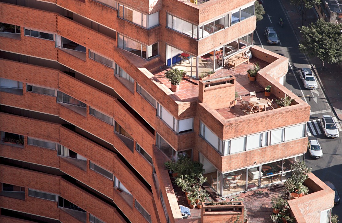 Aerial view of red-brick Park Towers in Bogotá showing stacked terraces with planted vegetation and geometric architectural design.