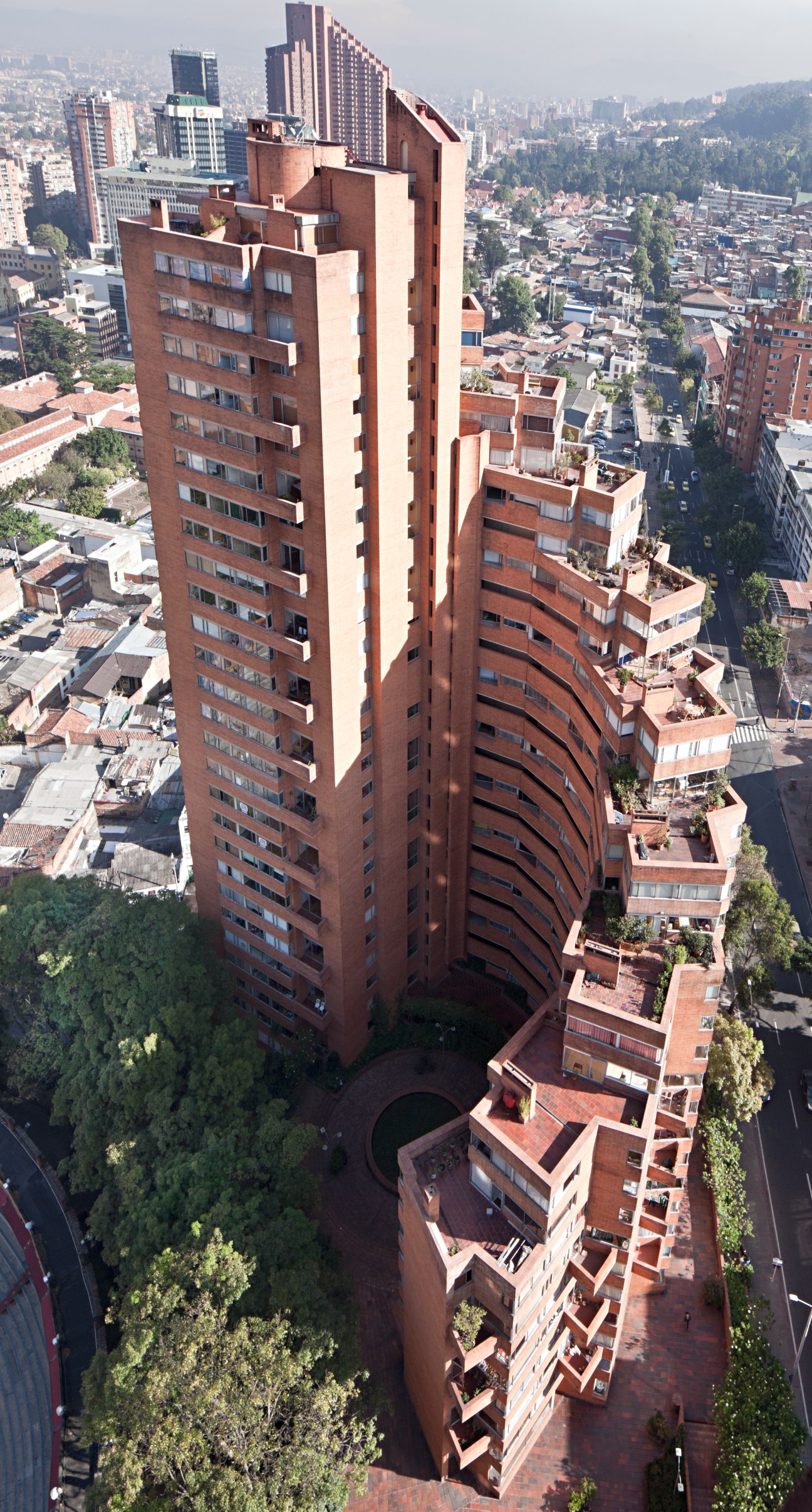 Aerial view of Park Towers' Tower C showing red-brick high-rise with stacked terraces overlooking Bogotá cityscape and mountains.
