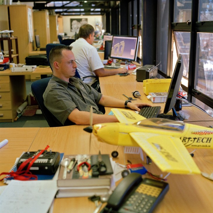 George Swanepoel, programmer at Aerosud, working at a computer in an office with aircraft models on the desk.