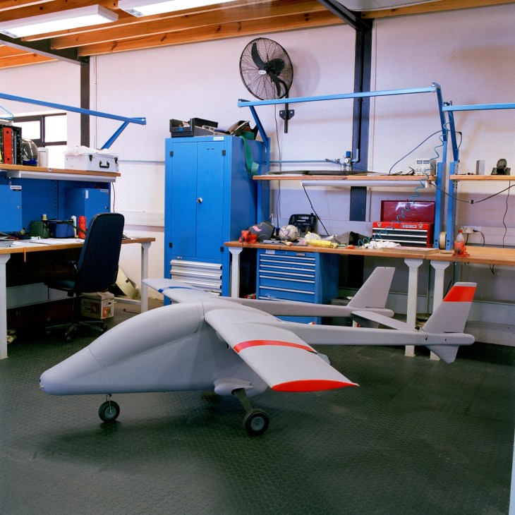 Scale model of the AHRLAC aircraft displayed in a workshop with blue workbenches and tools.
