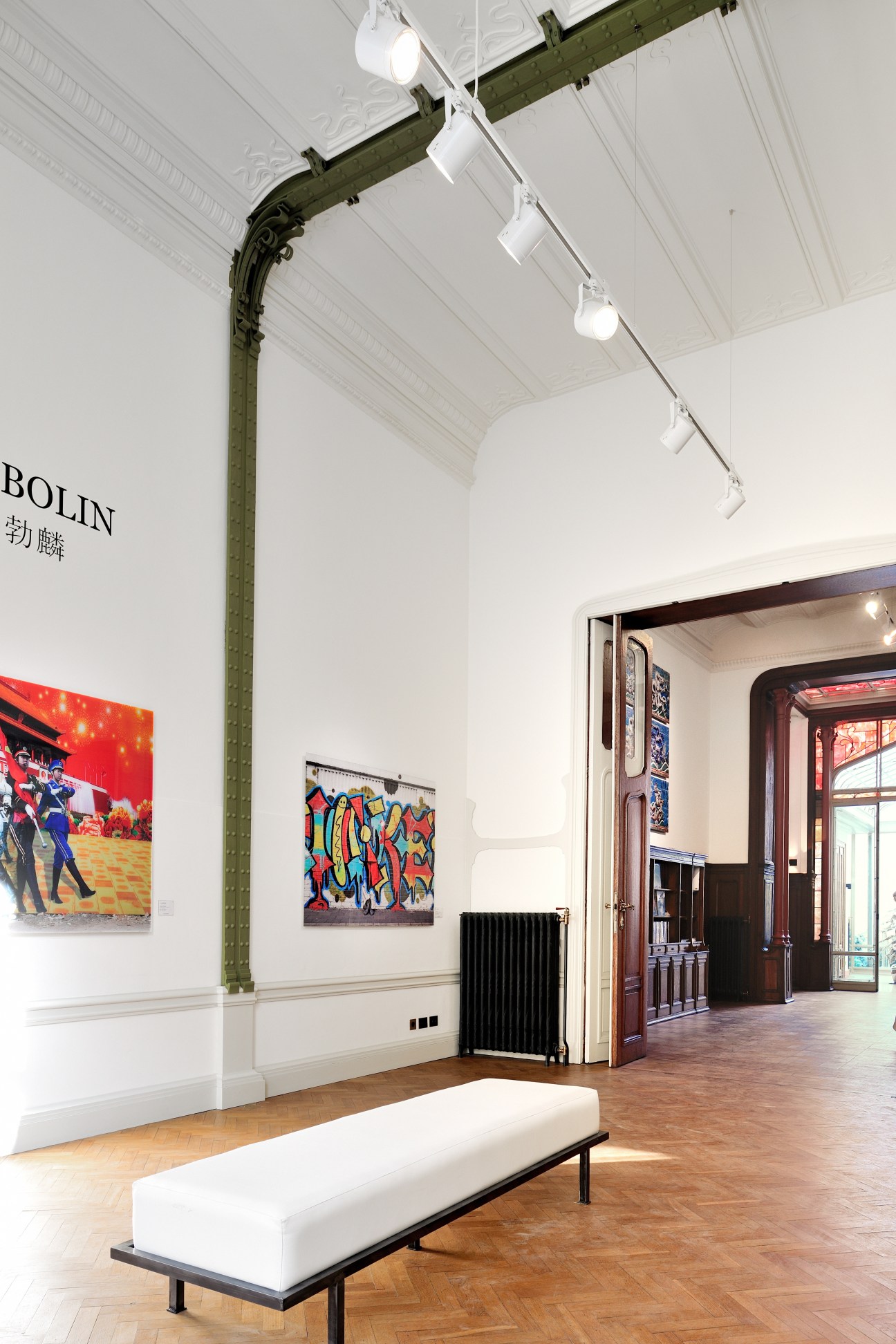Interior of Galerie Paris-Beijing Brussels showing contemporary artworks on white walls with ornate green architectural details and track lighting.
