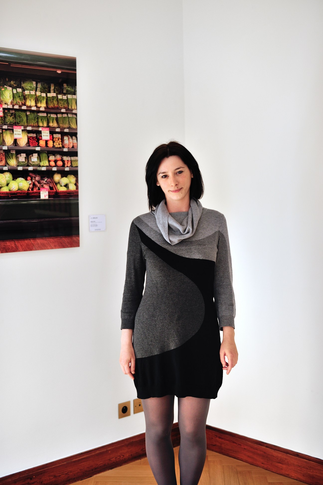 Woman standing in gallery space next to photograph of produce display.
