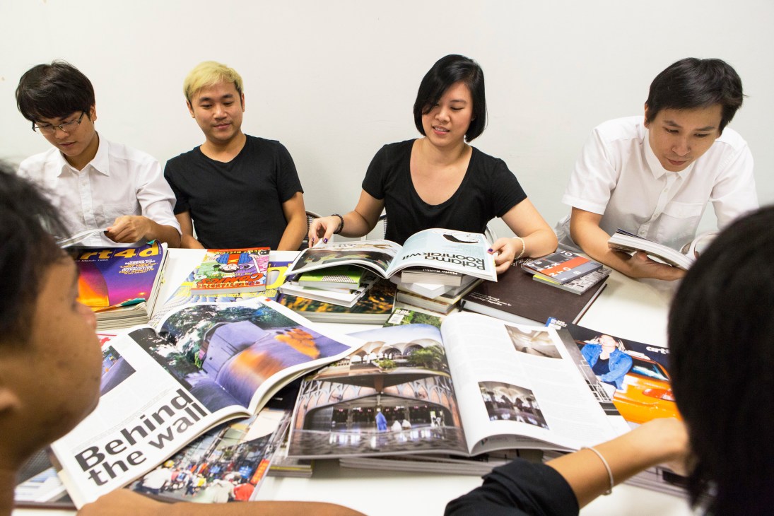 Five designers around white table examining open magazines and layouts during Art4d team meeting