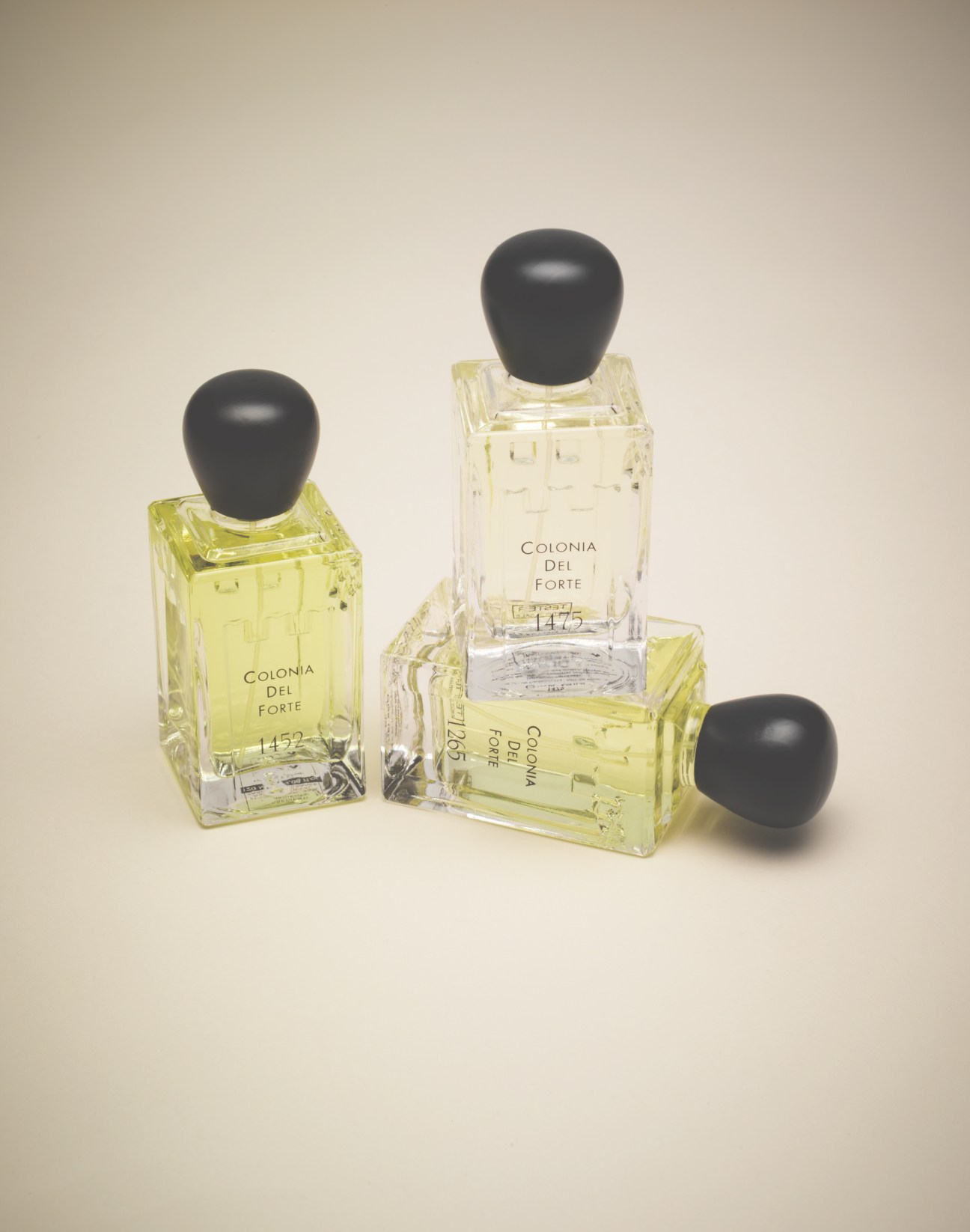 Three bottles of Profumi del Forte cologne with yellow liquid and black stoppers made of wenge wood.
