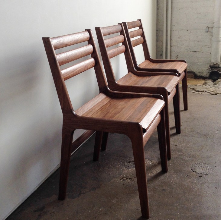 Three wooden chairs with curved backs and seats displayed in a concrete studio space.