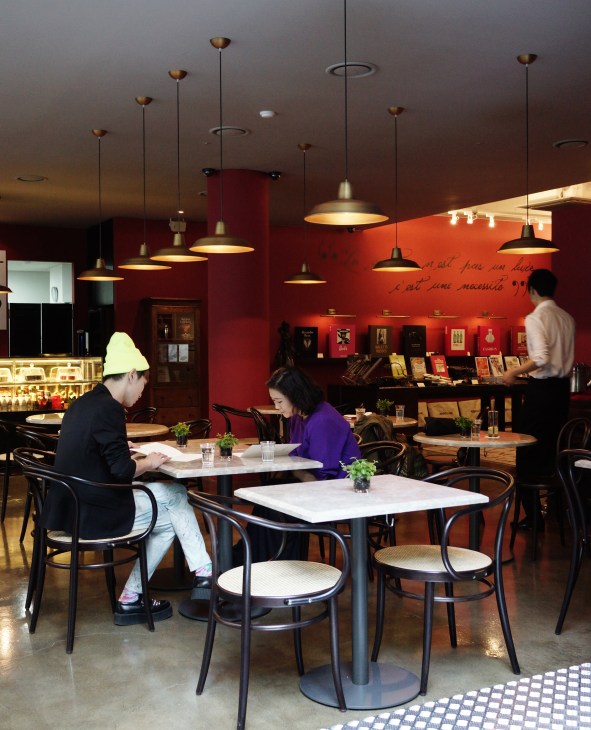 Interior of Assouline's Seoul cafe with scarlet walls, pendant lighting, and patrons dining at tables near bookshelves.