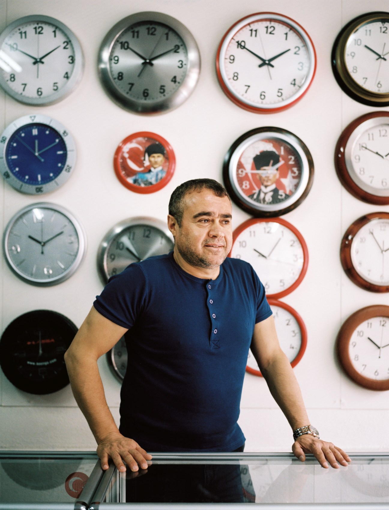 Osman Ulas stands in front of a wall displaying clocks, some featuring Ataturk's image, at his factory.