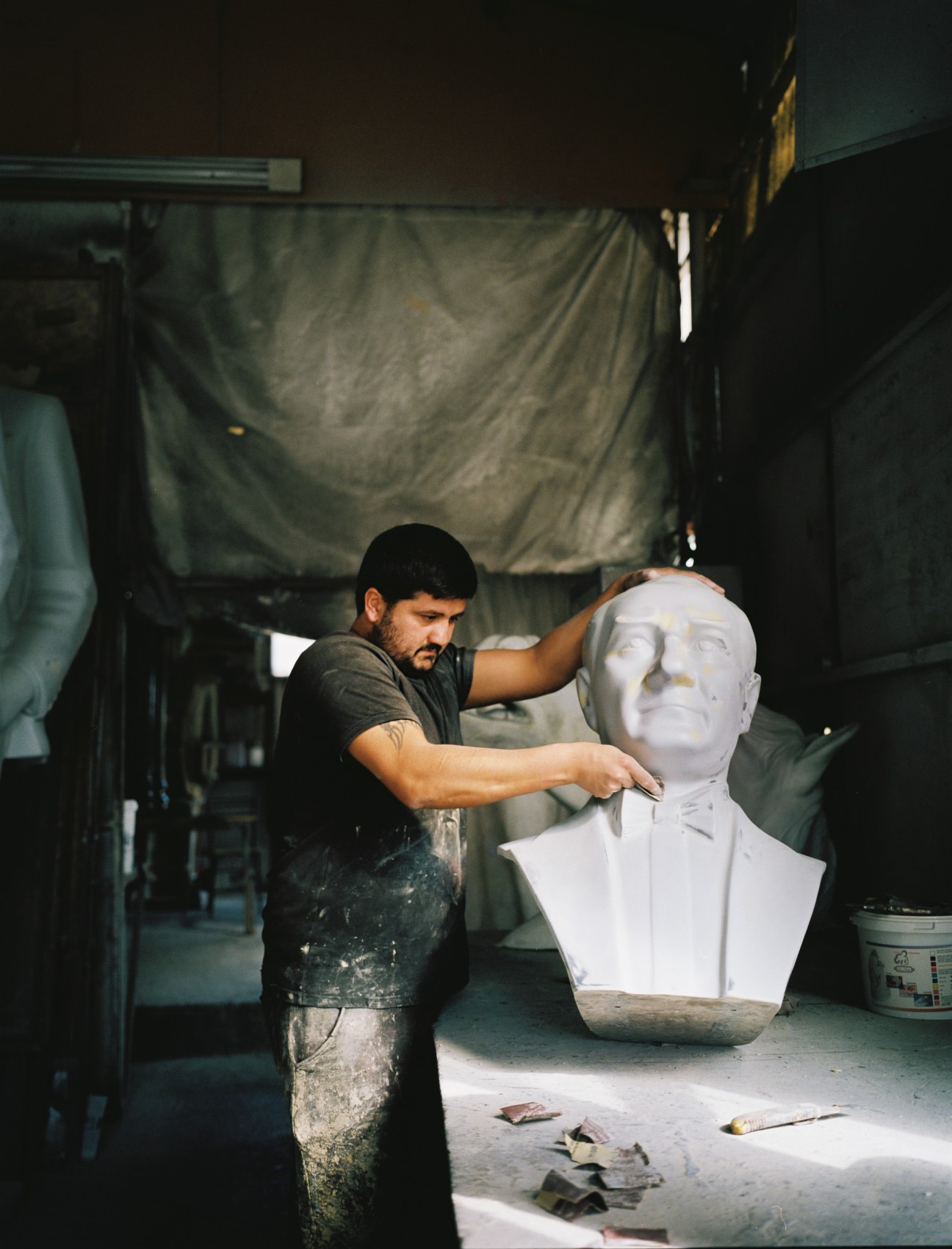 Studio worker sculpting a white bust of Mustafa Kemal Ataturk in a workshop.