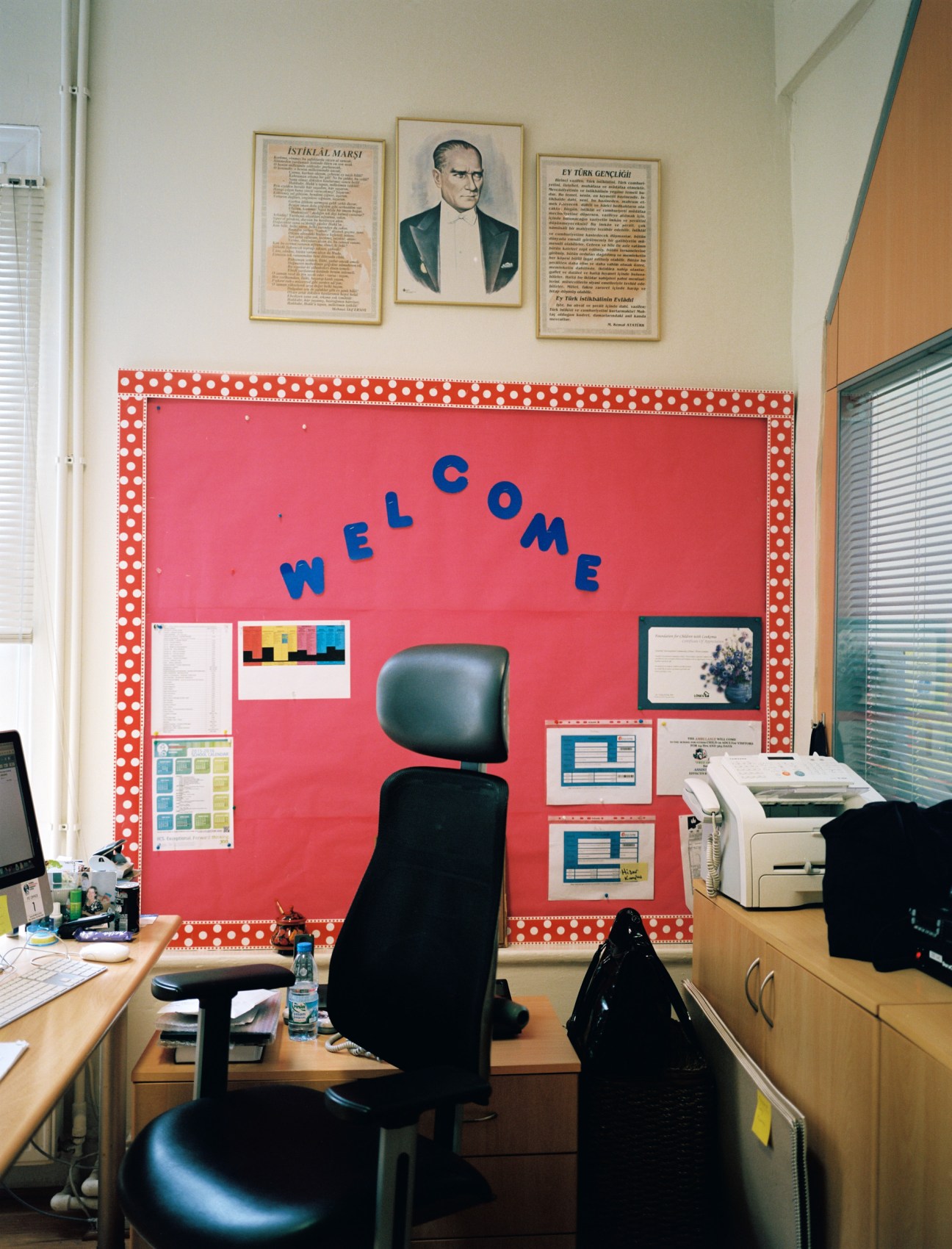 Classroom wall displaying framed portrait of Mustafa Kemal Ataturk above a red welcome bulletin board.
