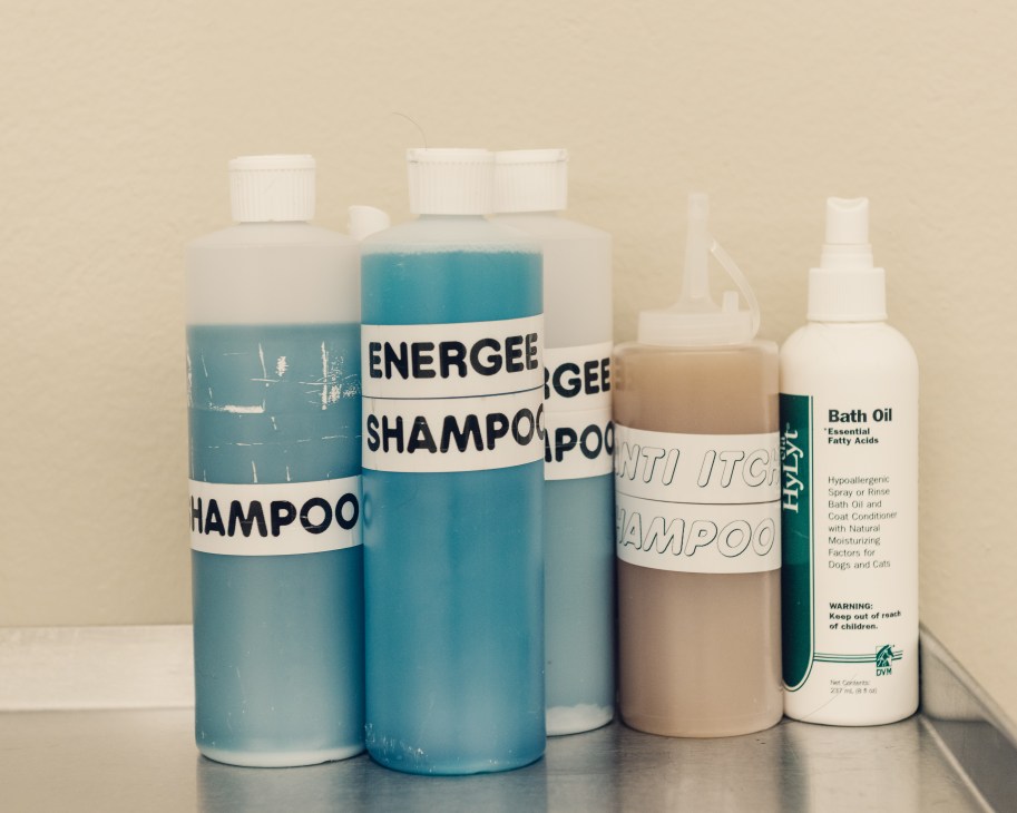 Dog grooming and hygiene products including shampoo bottles and bath oil arranged on a surface.