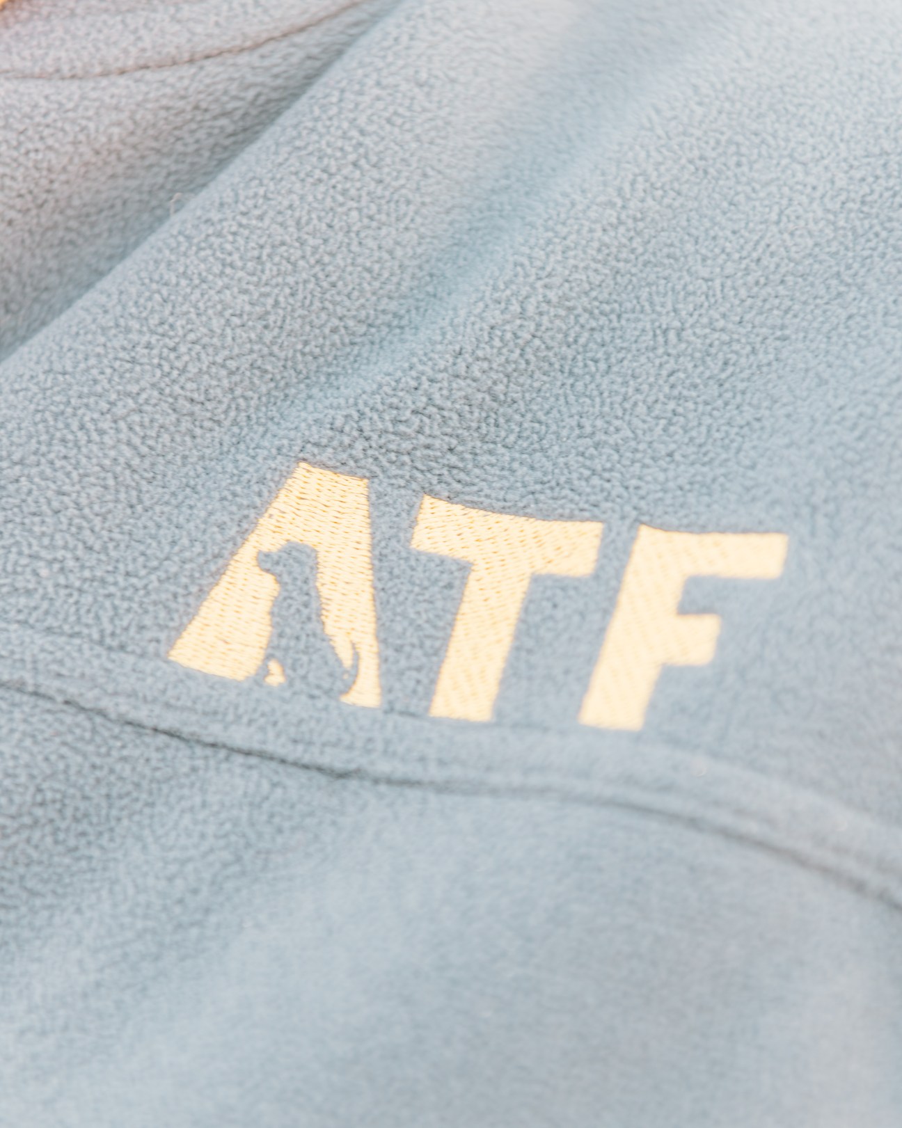 Gold ATF logo with dog silhouette embroidered on light blue fleece.