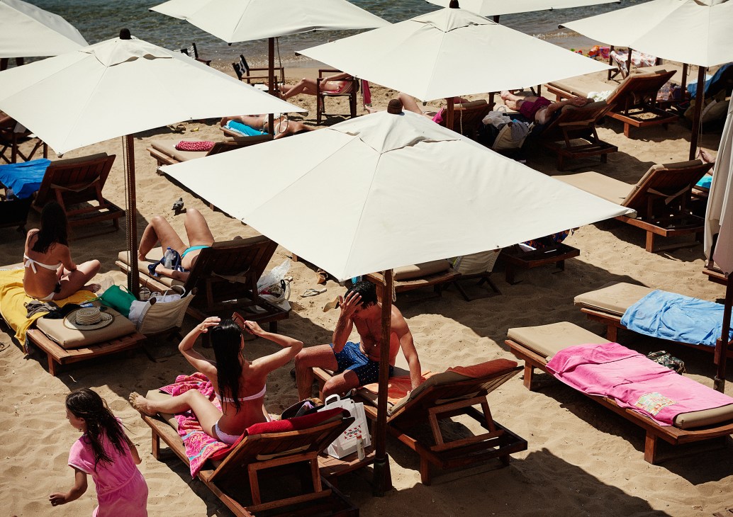 Beachgoers relax on sun loungers under white umbrellas at Astir Beach in Athens.