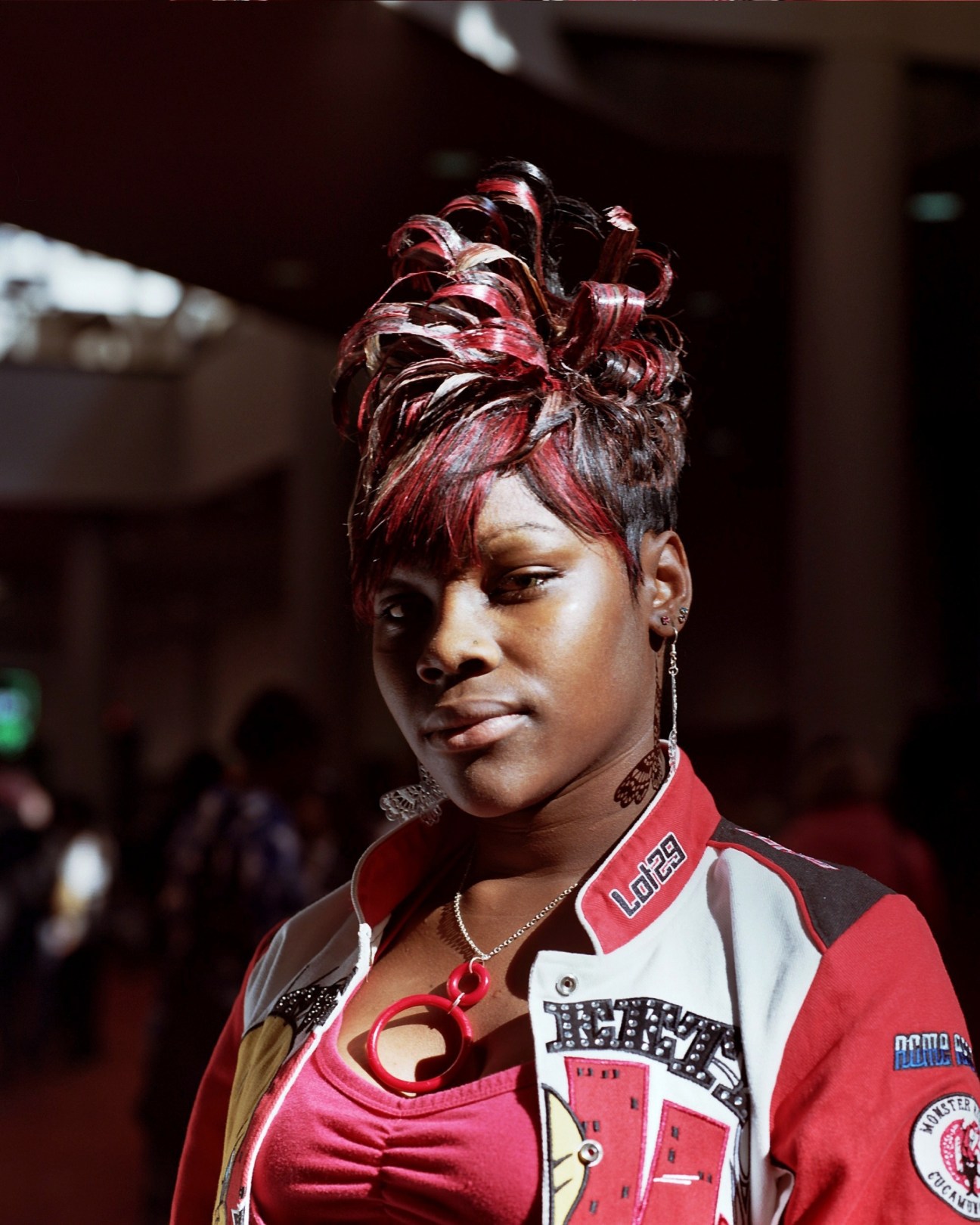 Woman with burgundy and black upswept hairstyle wearing red and white jacket at hair show.